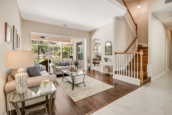 Spacious and modern living room with a staircase, featuring a comfortable seating area, decorative table, and large windows overlooking a backyard.